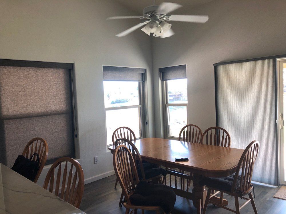 Dining room with wooden table, six chairs, windows, and ceiling fan.