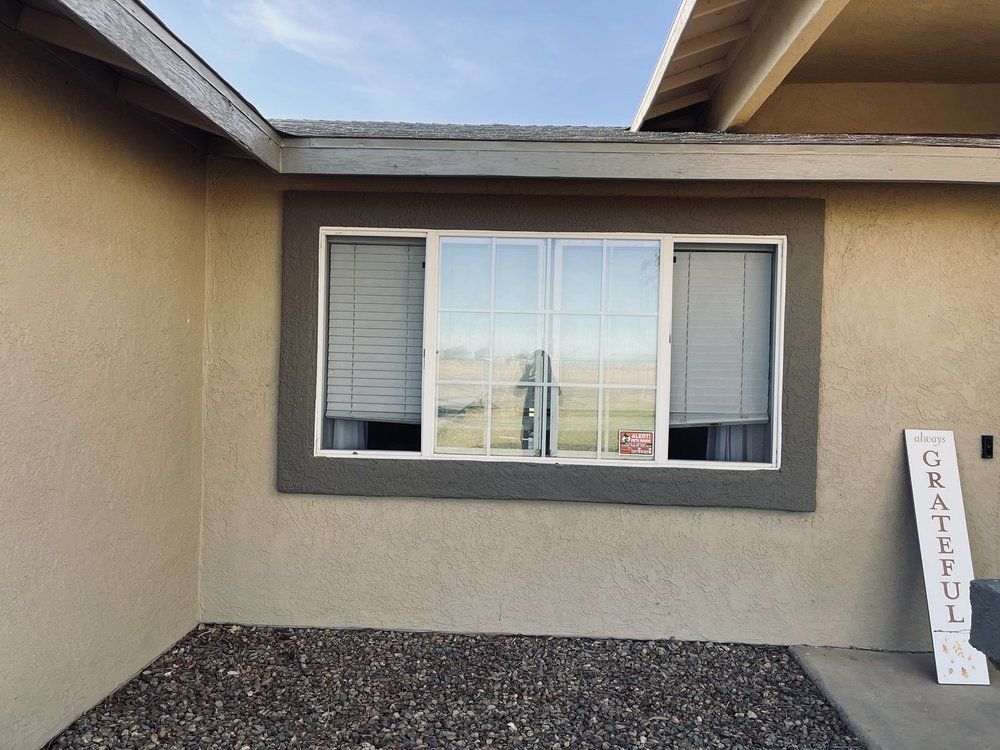 Window with white blinds, reflecting a field. The window has a gray trim, set in a tan wall.