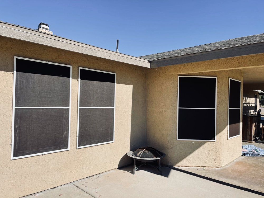 Exterior view of beige stucco house with several windows covered with black screens.