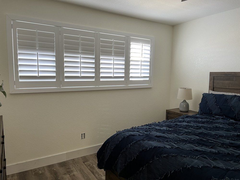 Bedroom with a bed, nightstand, and window with shutters. Walls are beige, bedspread is blue.