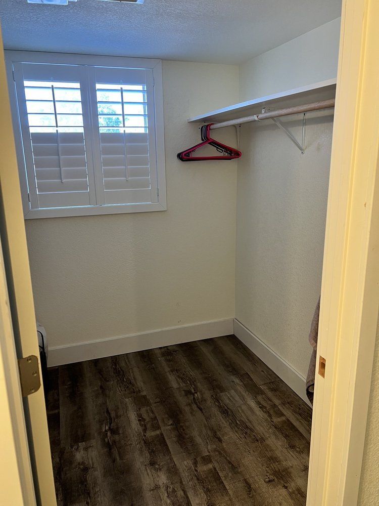 Empty closet with wood-look flooring, white walls, and a window with closed shutters.