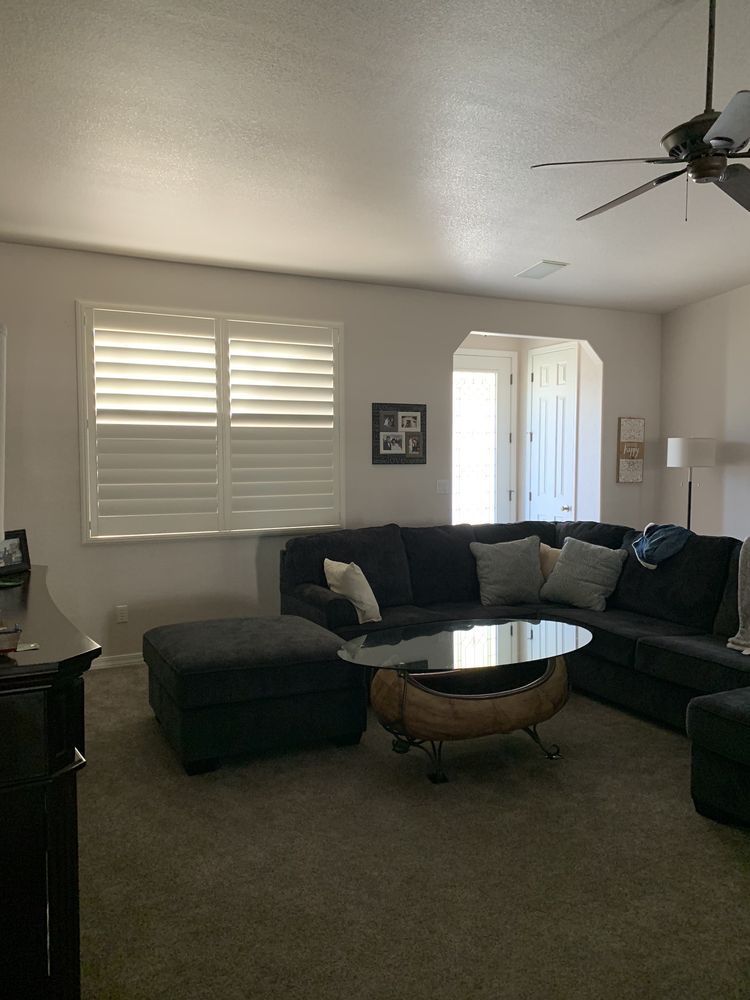 Living room with gray sectional sofa, ottoman, and round coffee table. White shutters and door.