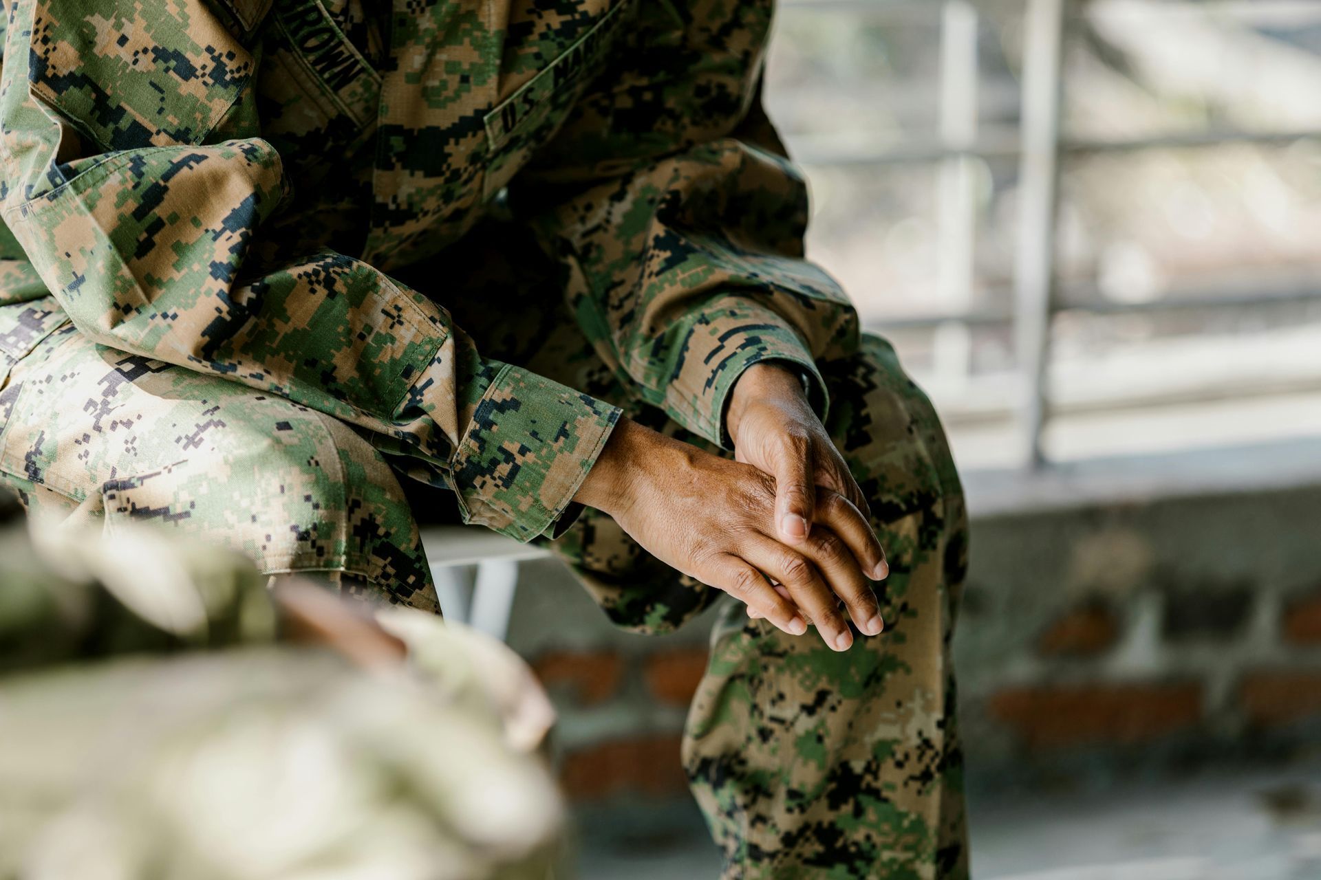 A soldier is sitting on a bench with his hands on his knees.