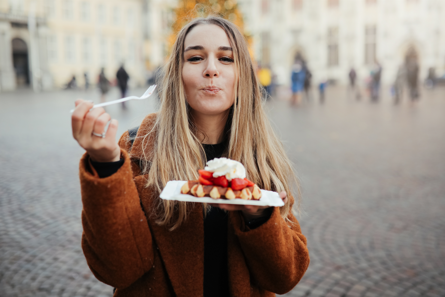 Une femme mange une gaufre avec des fraises et de la crème fouettée avec une fourchette.
