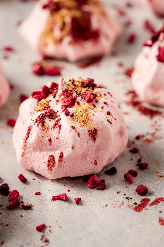 Un gros plan d'une meringue rose avec des framboises sur une table.