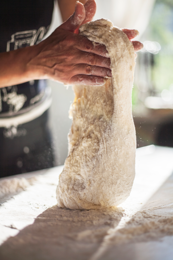 Une personne pétrit de la pâte sur une table.