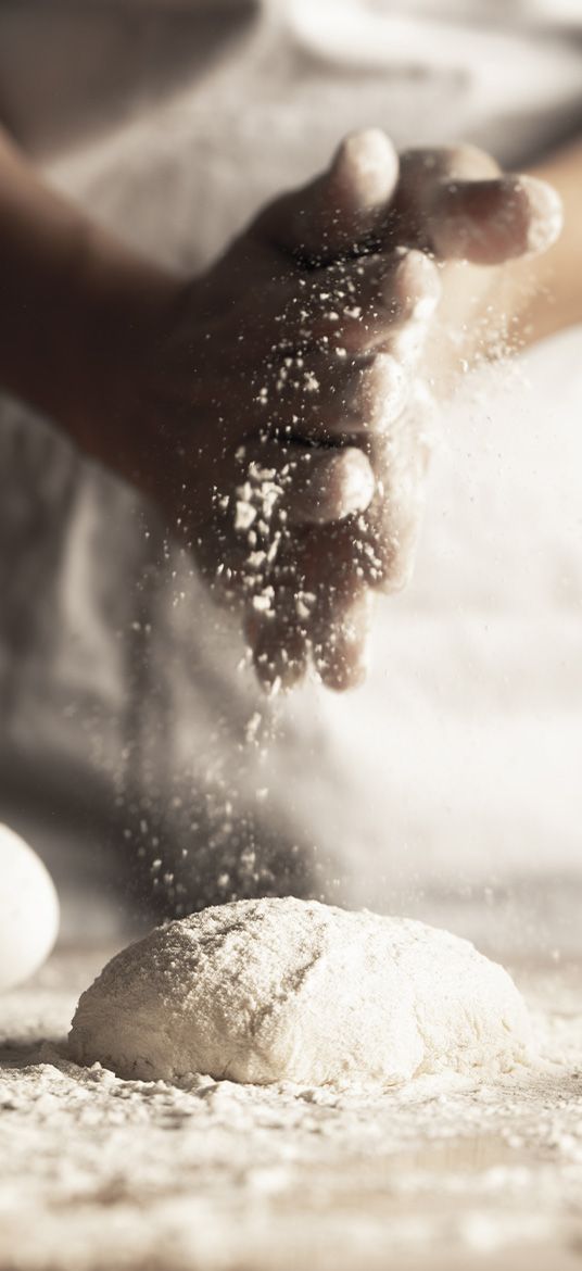Une personne saupoudre de farine sur une boule de pâte.