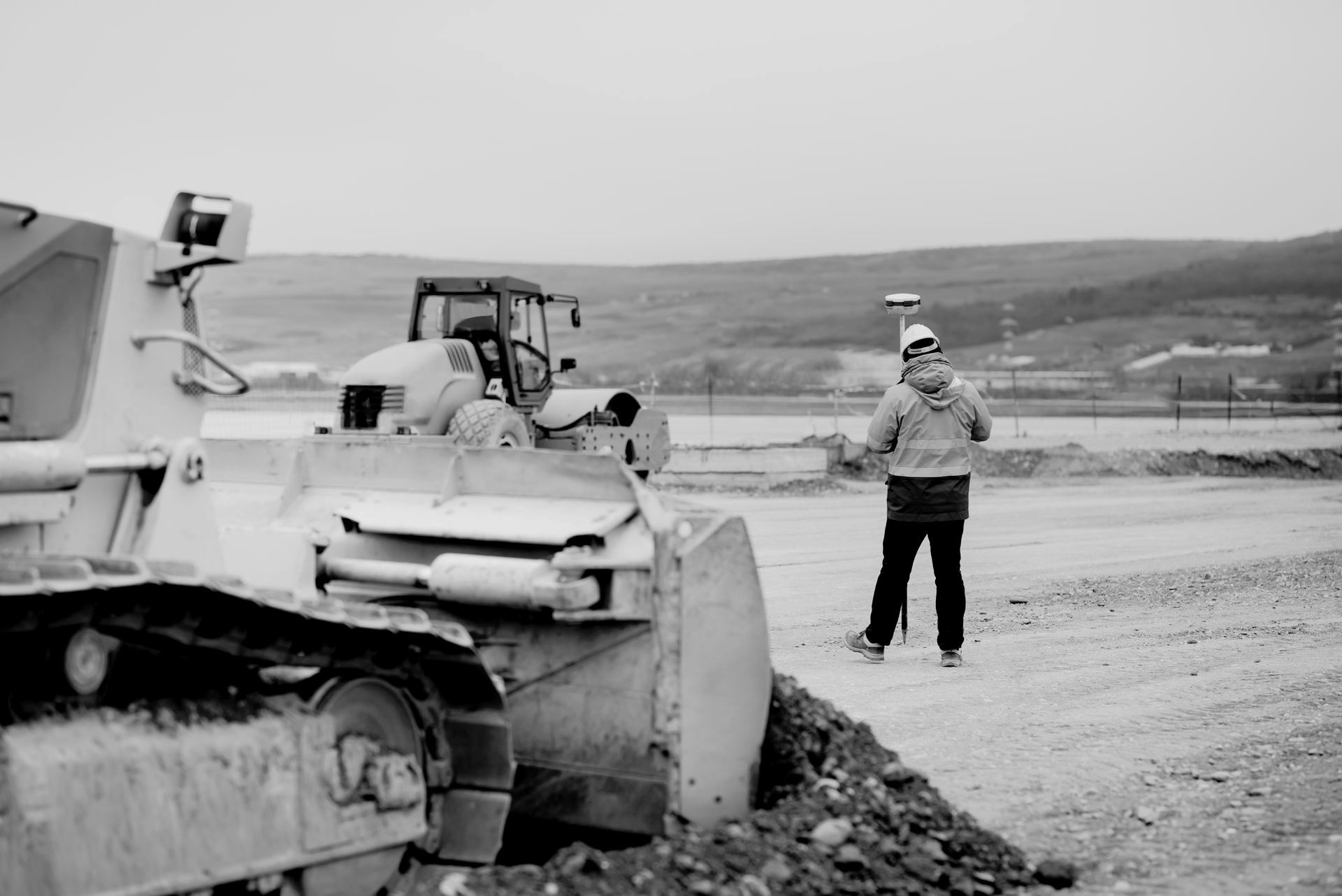 Surveyor with GPS equipment near bulldozer at a construction site; overcast day.
