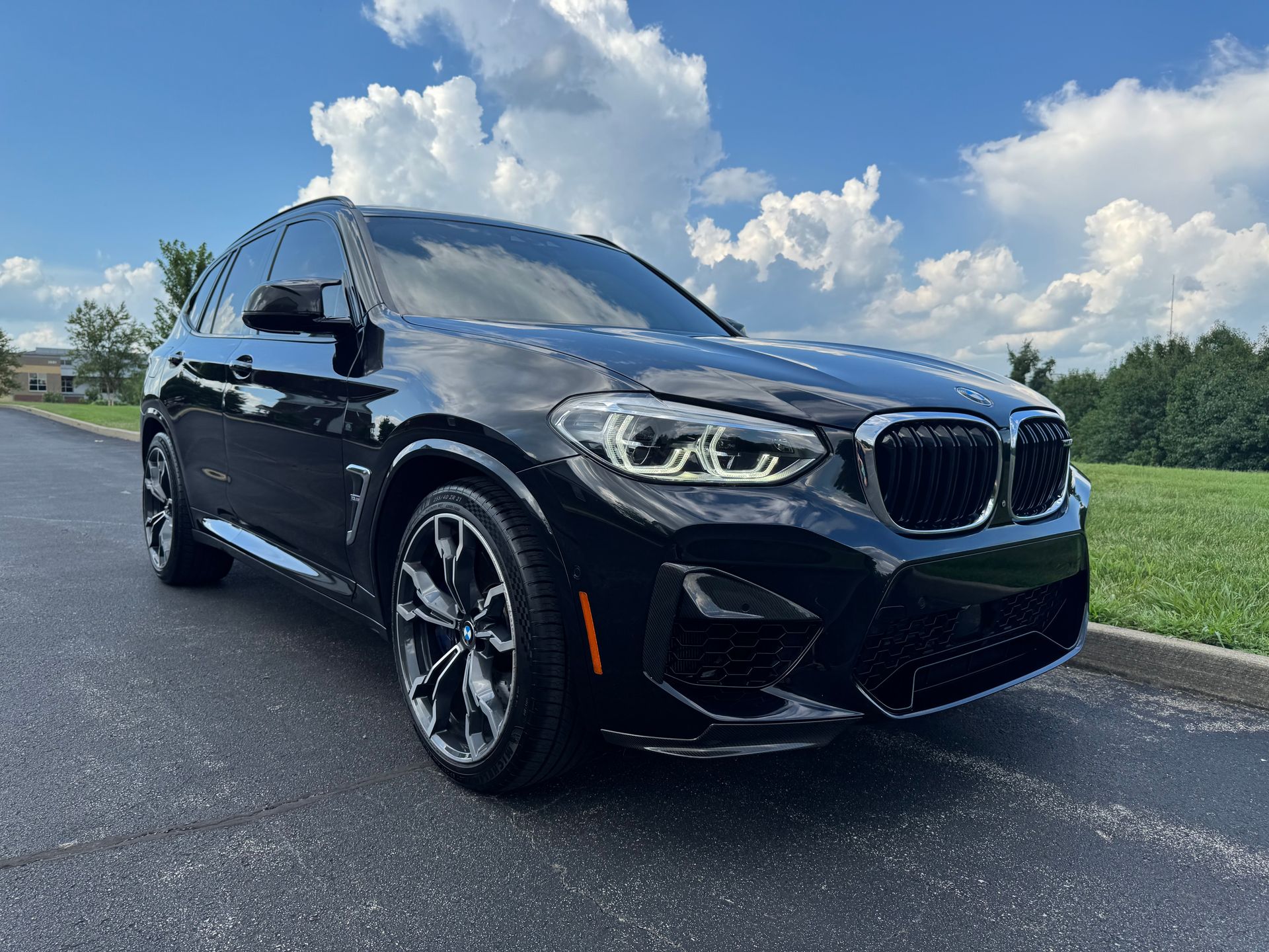 Black BMW X3 SUV parked on asphalt in front of a green lawn and cloudy blue sky.