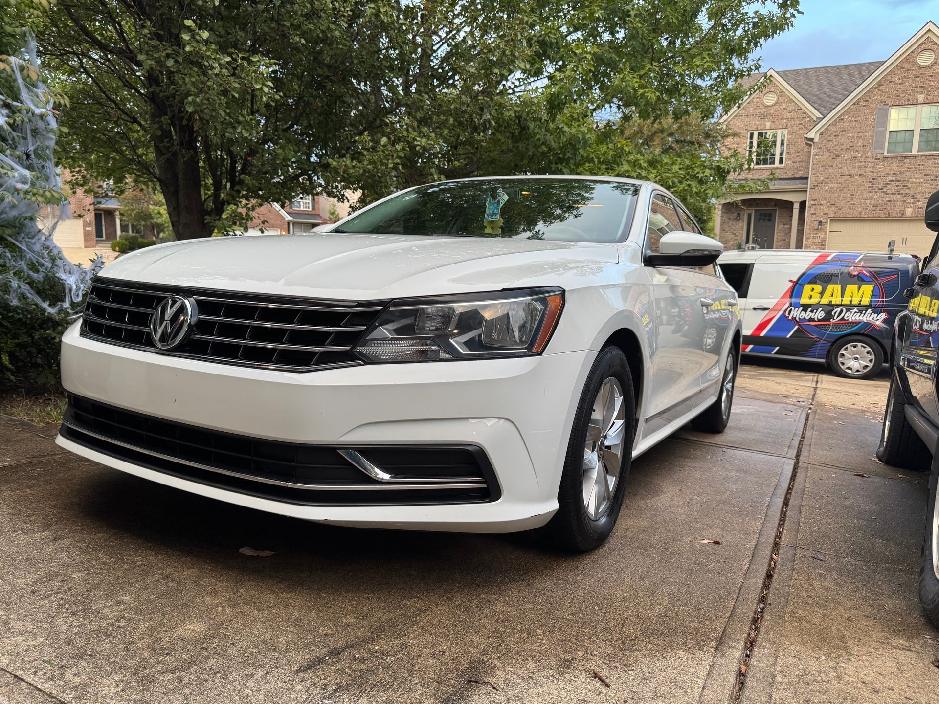 White Volkswagen Passat parked on a paved driveway in front of a house.