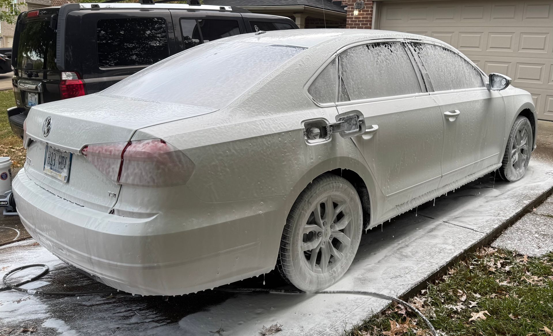 White car covered in foamy soap suds during a car wash in a driveway.