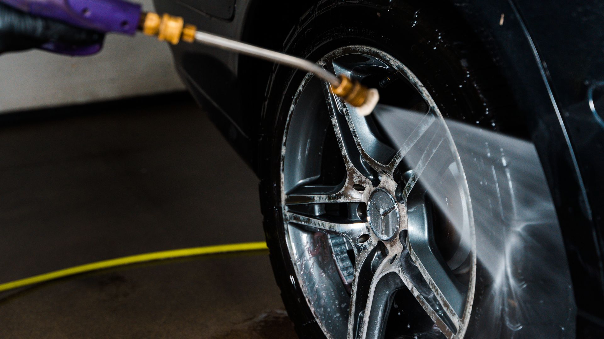 Washing a car wheel with a high-pressure nozzle, spraying foamy cleaner.