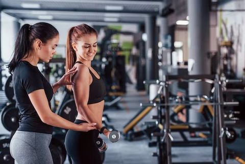 A woman is helping another woman lift a barbell in a gym.