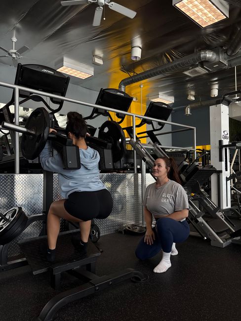 A woman is helping another woman lift a barbell in a gym.