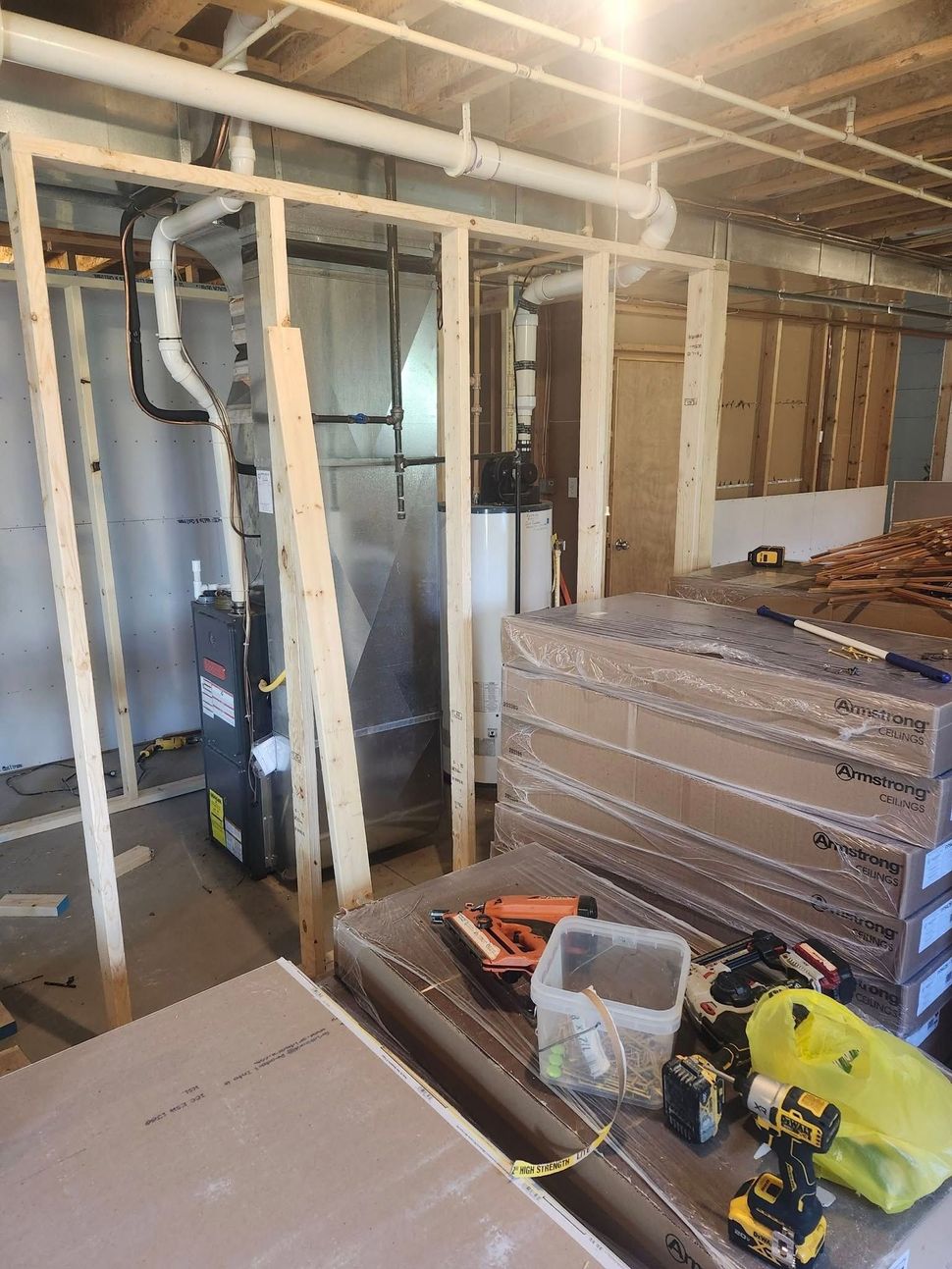 A basement under construction with a furnace and a stack of drywall.