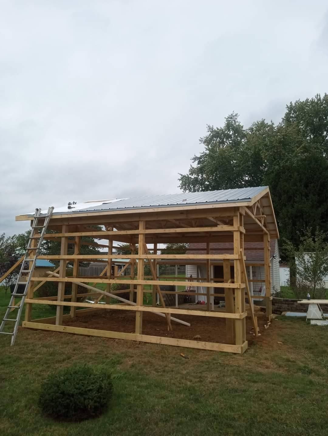 A wooden structure with a metal roof is being built in a backyard.