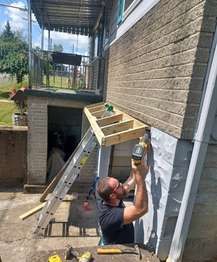 A man is using a drill to install a wooden structure on the side of a building.