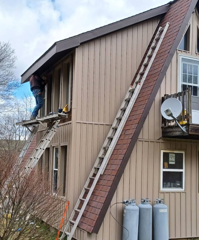 A man is standing on a ladder on the side of a house.
