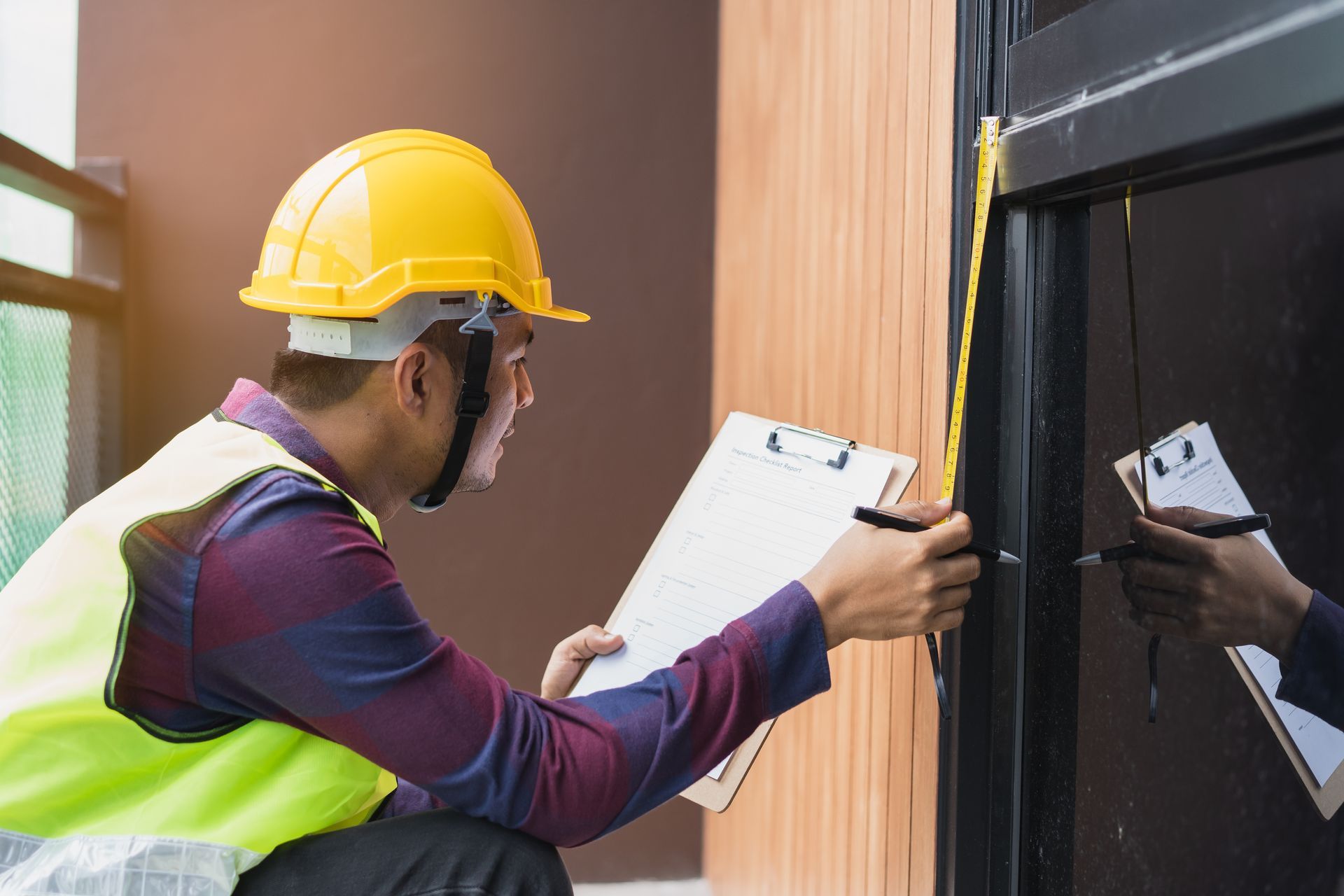 A construction worker is measuring a door with a tape measure and writing on a clipboard.