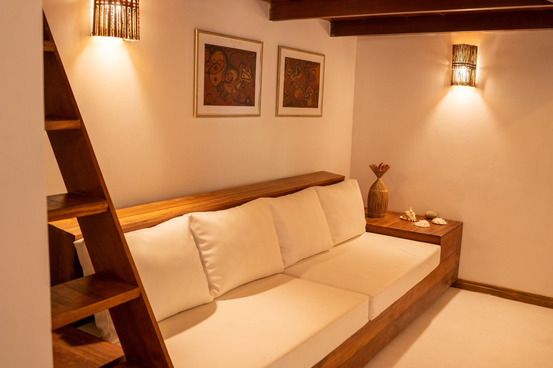 Uma sala de estar com um sofá, escadas e dois quadros na parede.