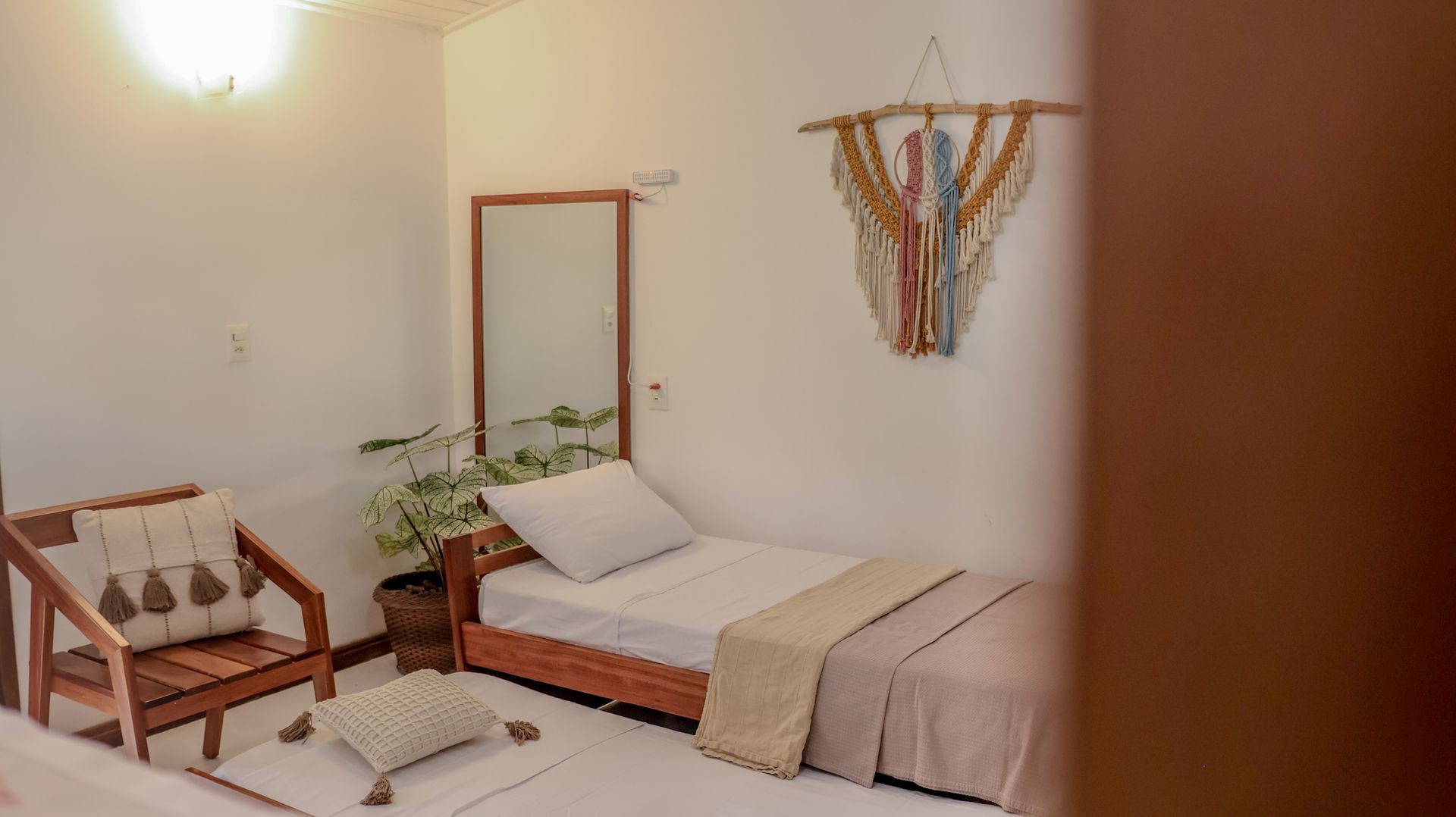 Quarto com duas camas, uma cadeira de madeira e um quadro pendurado em uma parede branca.