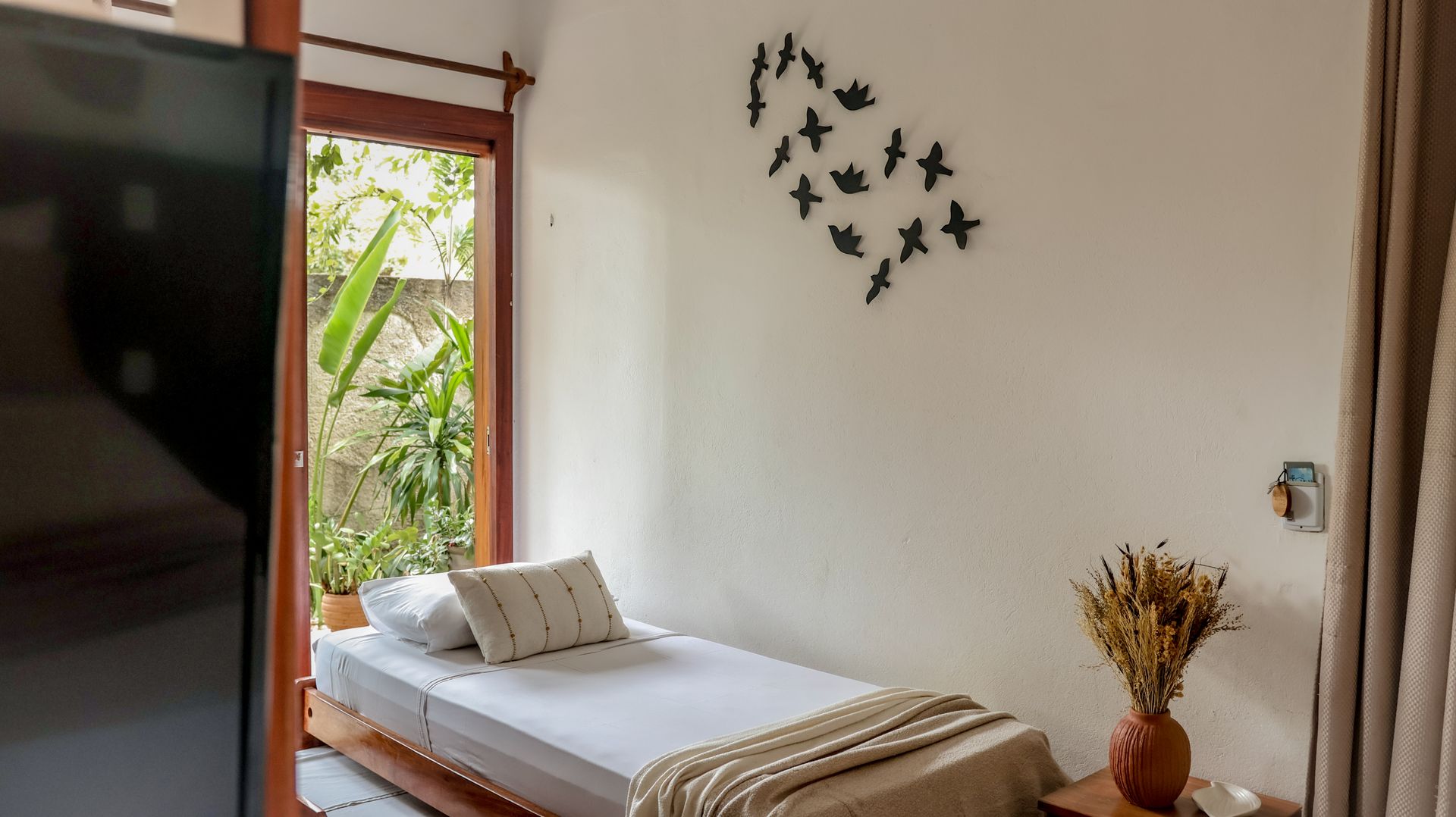 Quarto com duas camas de solteiro, porta aberta para a vegetação, borboletas na parede e um vaso com flores.