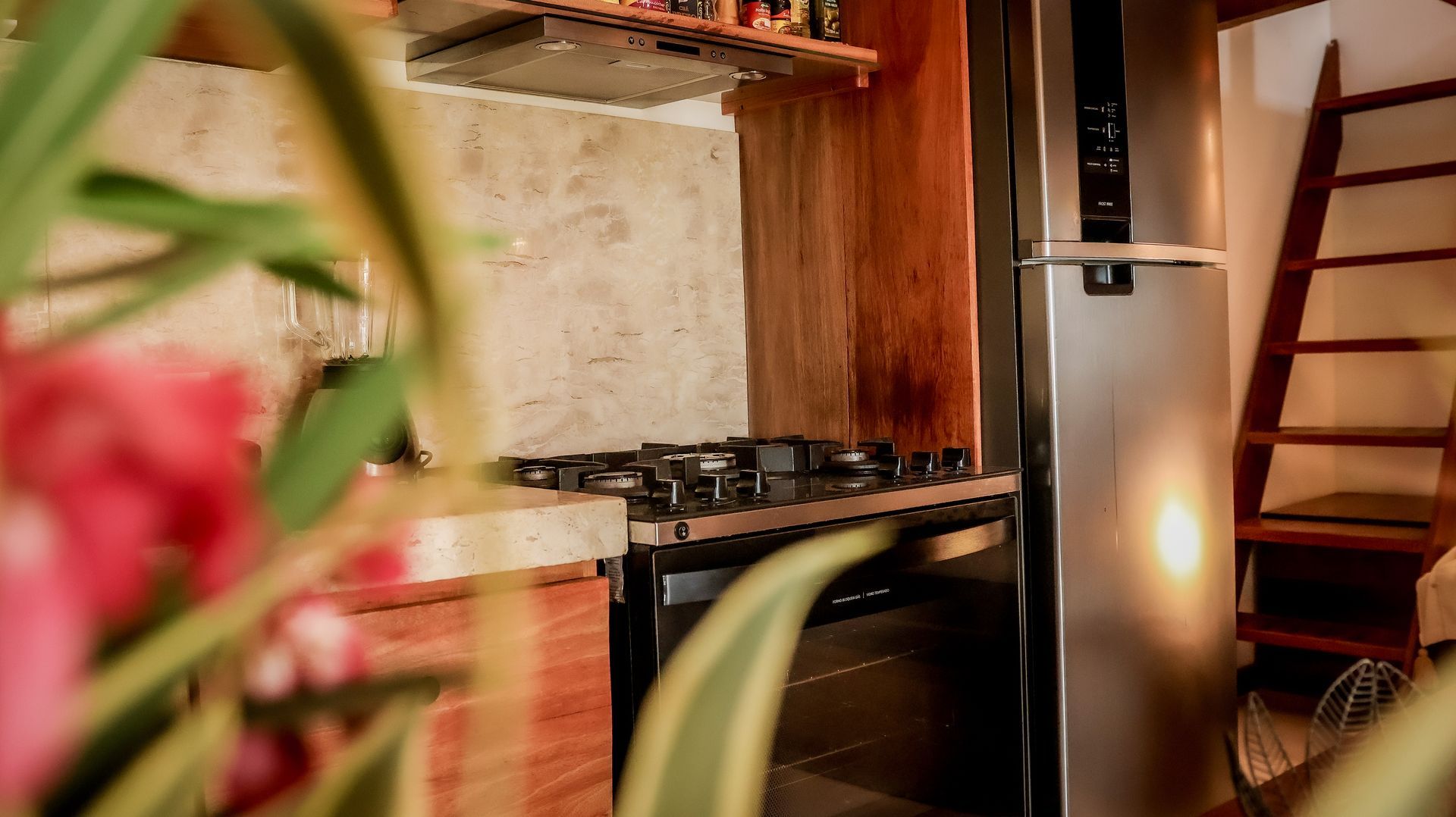 Cozinha com fogão e geladeira de aço inoxidável. Uma escada de madeira está encostada na parede.