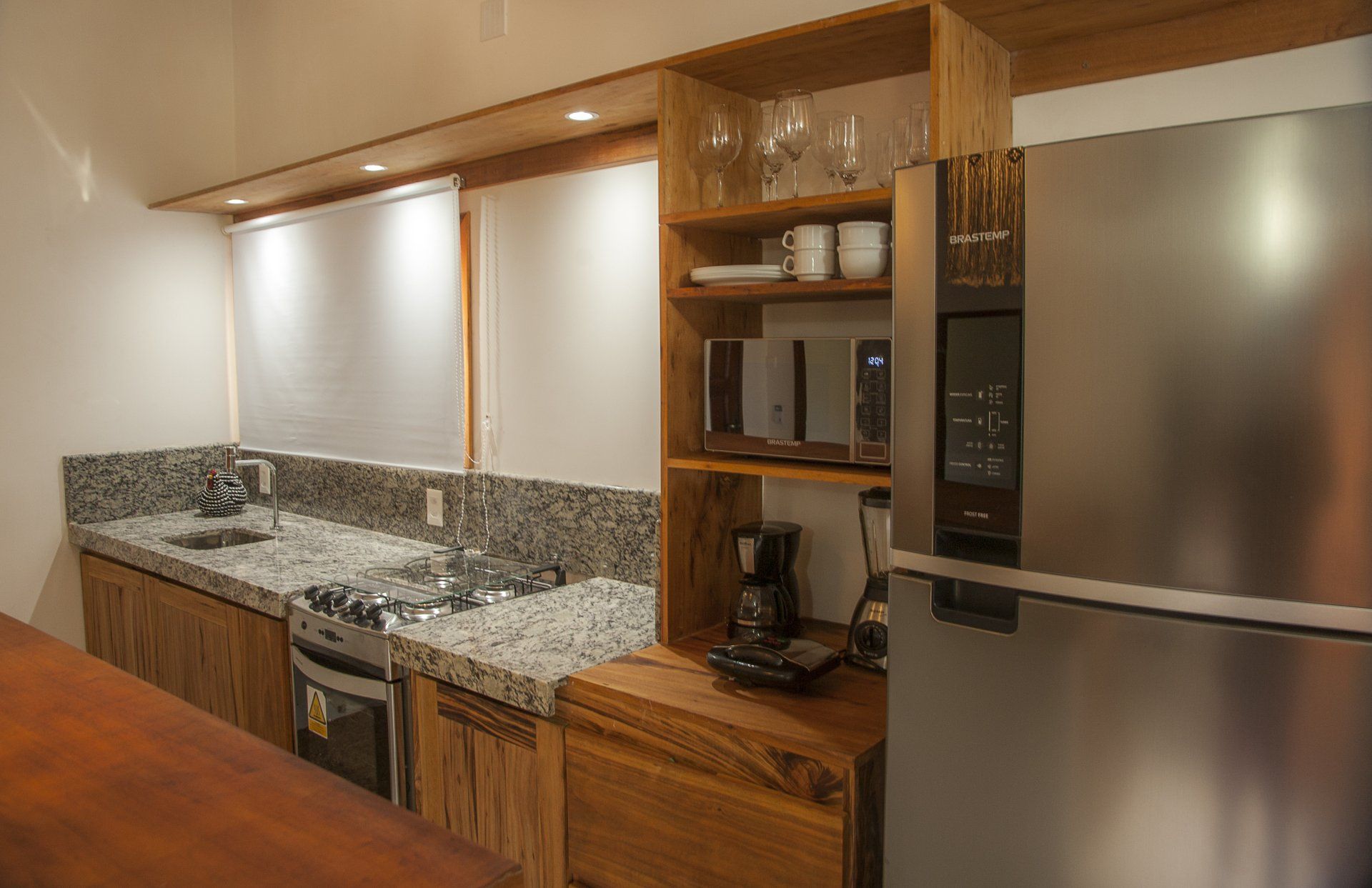 Uma cozinha com eletrodomésticos de aço inoxidável, bancadas de granito, geladeira, micro-ondas e pia.