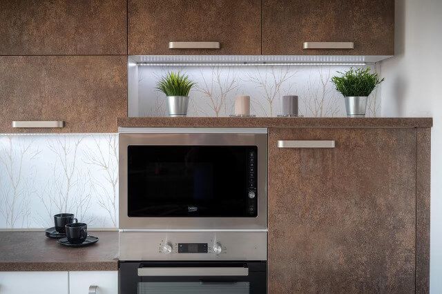 A kitchen with stainless steel appliances , wooden cabinets , and a microwave oven.