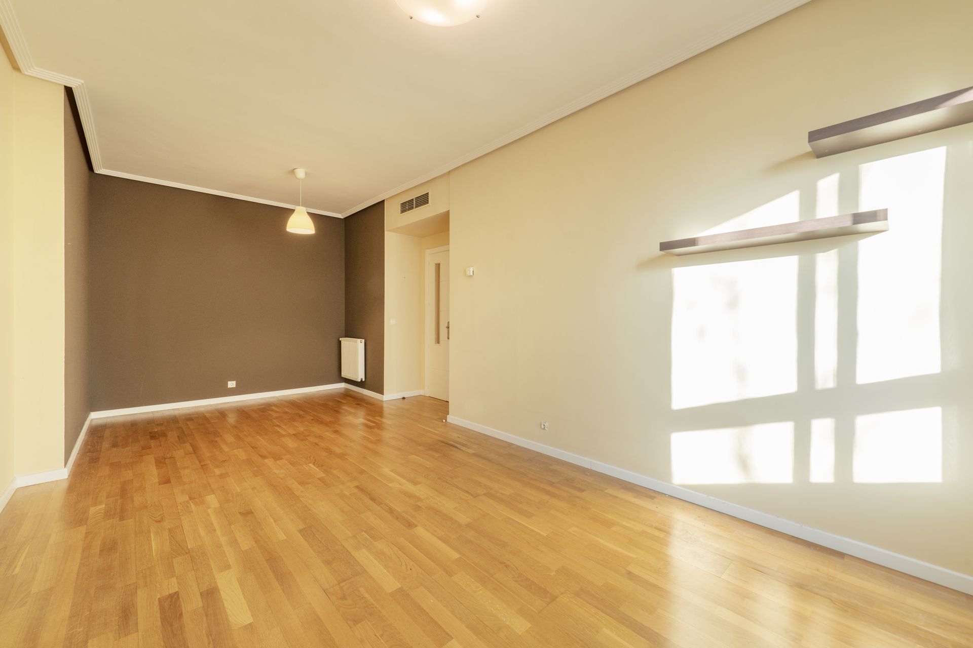 Empty room with hardwood floors, a brown accent wall, and a window letting in sunlight.