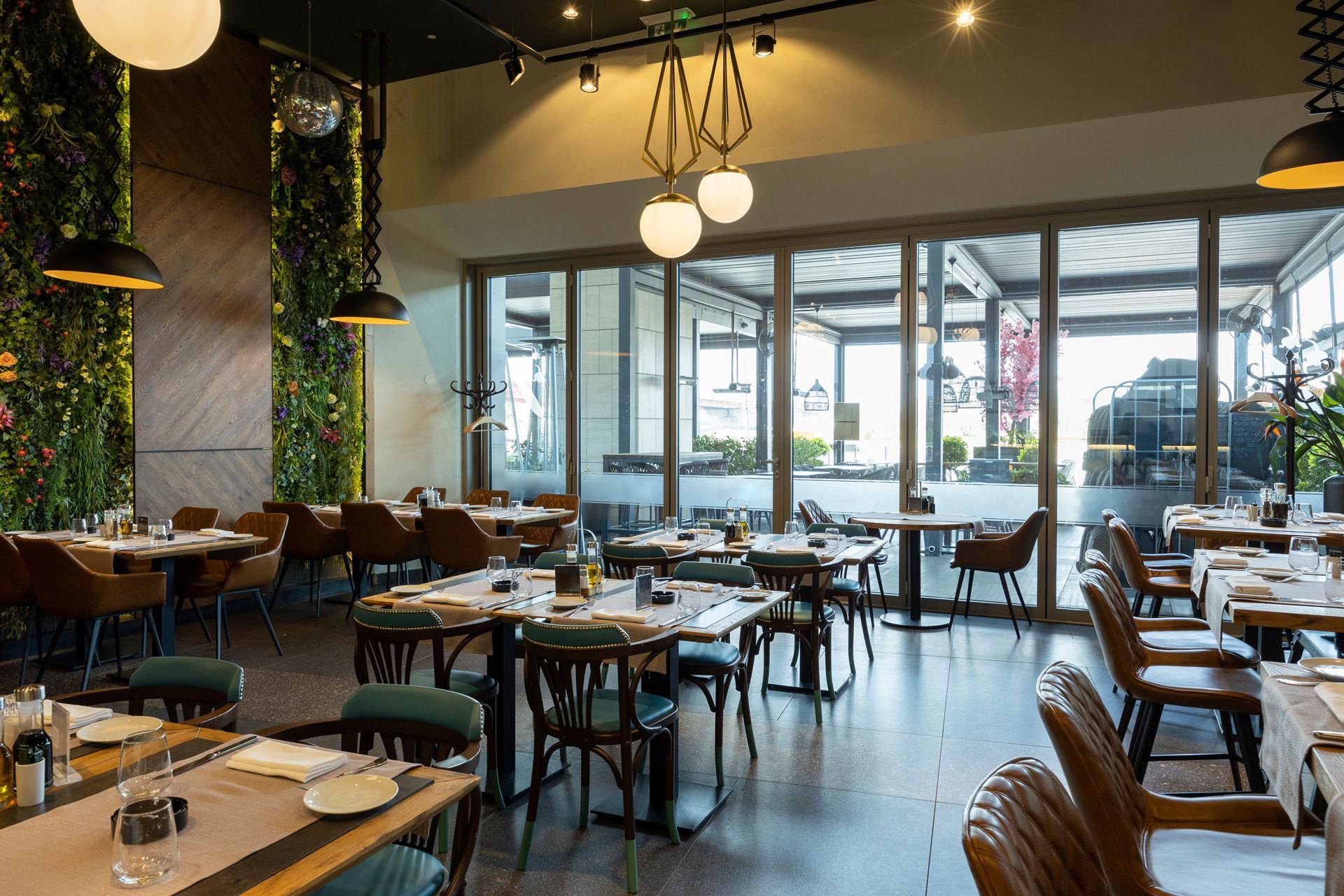 Restaurant interior with tables set for dining, large windows, and a green wall.