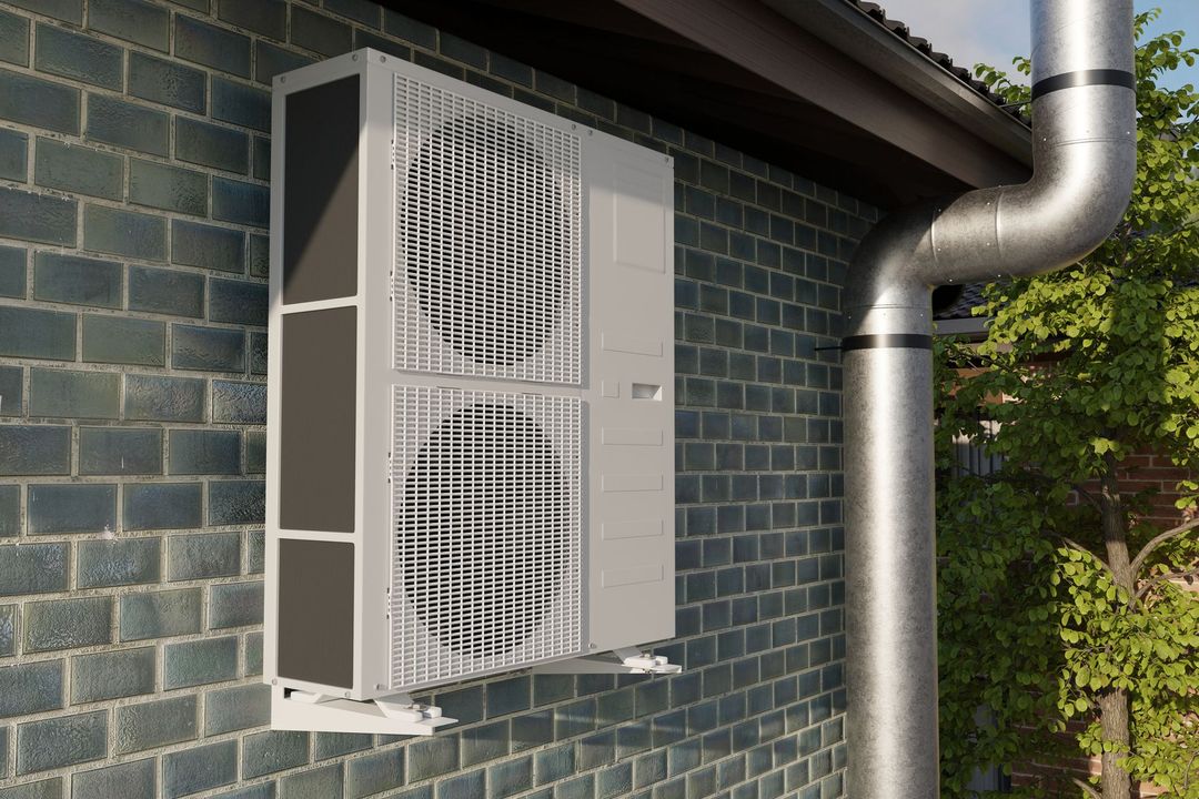 Un'unità esterna di una pompa di calore di colore grigio chiaro, montata su un muro di mattoni scuri accanto a un grande tubo di scarico metallico.