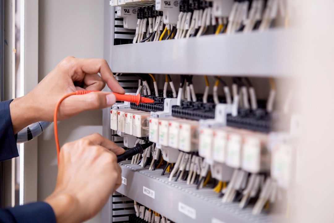 Un tecnico utilizza un multimetro con sonde rosse e nere per testare i collegamenti su un circuito stampato all'interno di un quadro elettrico.