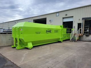 A large green dumpster is parked in front of a building.