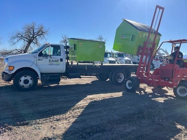 A white truck is being towed by a red forklift.