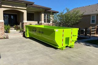 A large green dumpster is parked in front of a house.