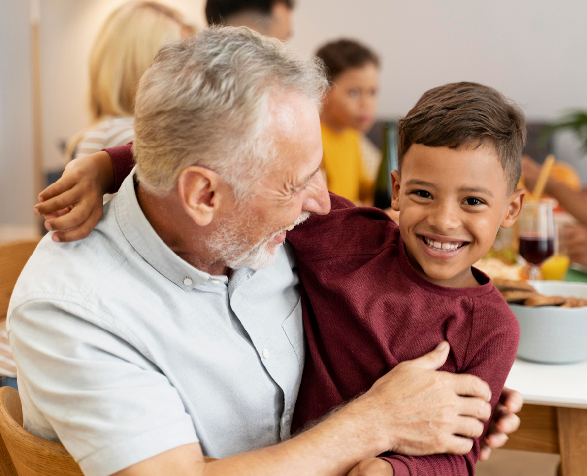 Abuelo abrazando a un niño sonriente en una cena familiar.