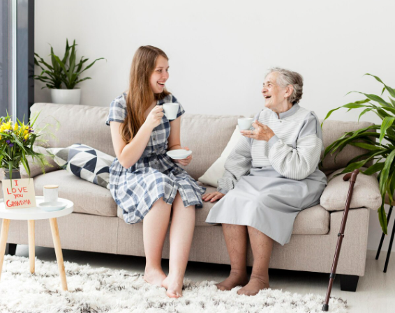 Una mujer joven y una anciana se ríen mientras beben té en un sofá.