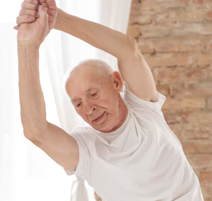 Un hombre mayor con una camisa blanca se estira, extendiendo un brazo por encima de la cabeza y hacia un lado