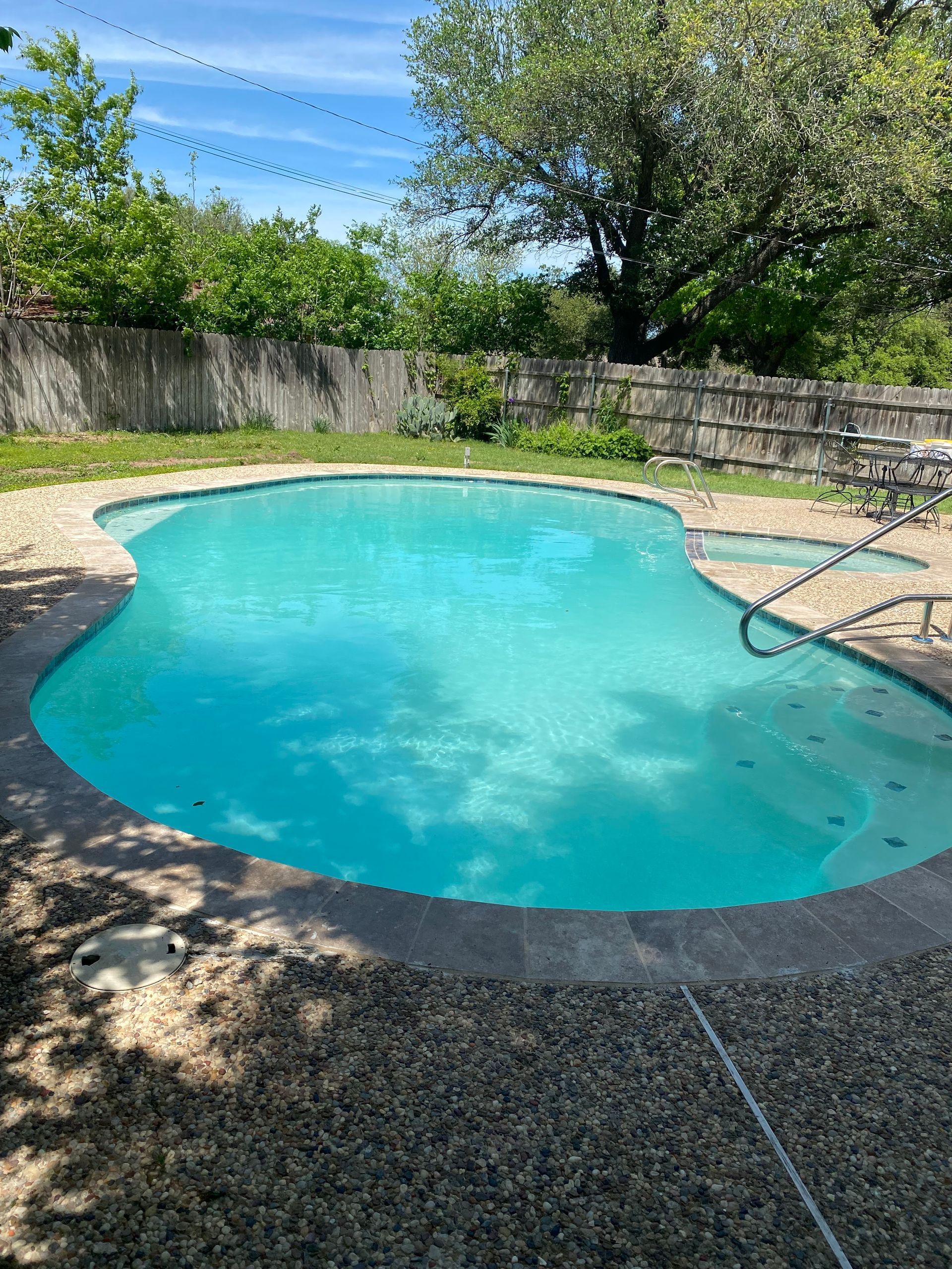 A large swimming pool in a backyard with a fence and trees in the background.