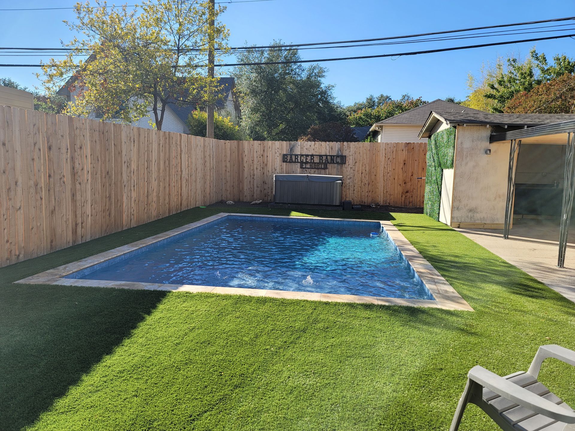 A large swimming pool is surrounded by a wooden fence in a backyard.