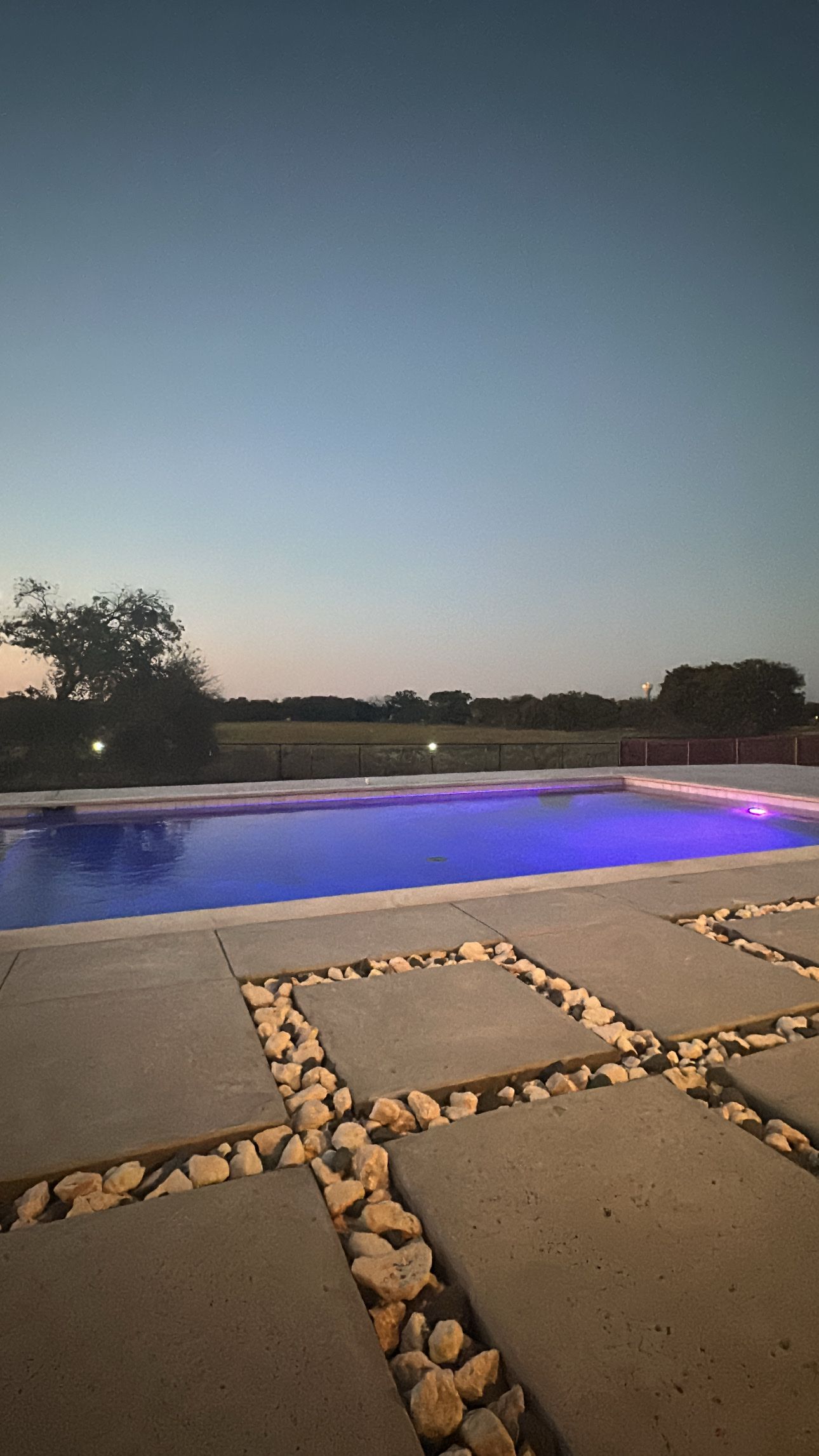 A large swimming pool is lit up at night with purple lights.