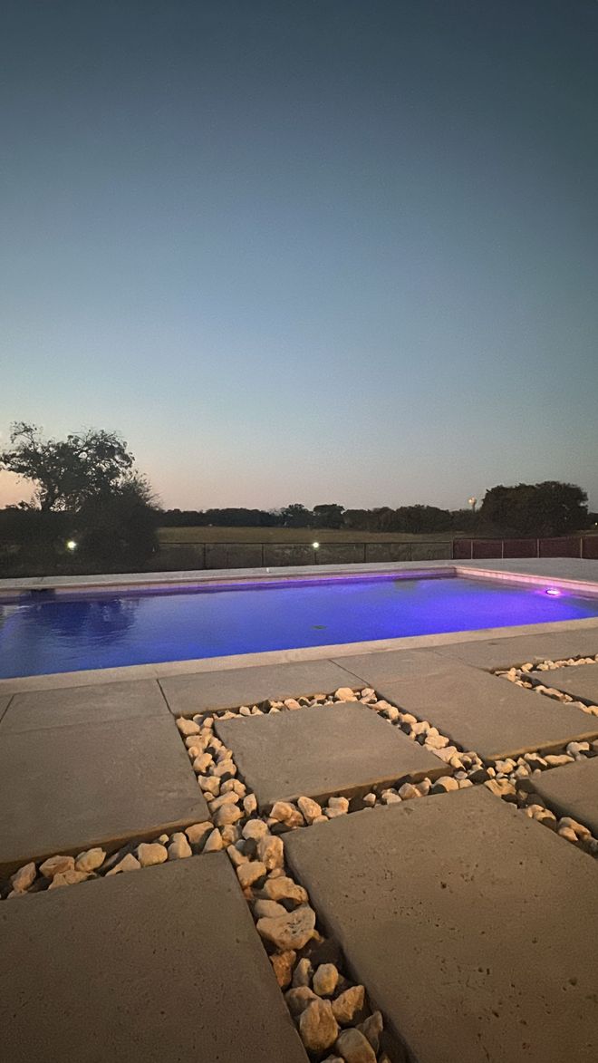 A large swimming pool is lit up at night with purple lights.