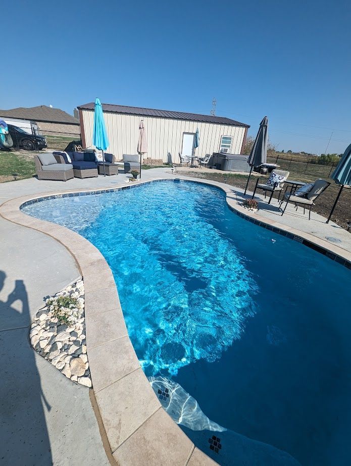 A large swimming pool surrounded by chairs and umbrellas in front of a house.