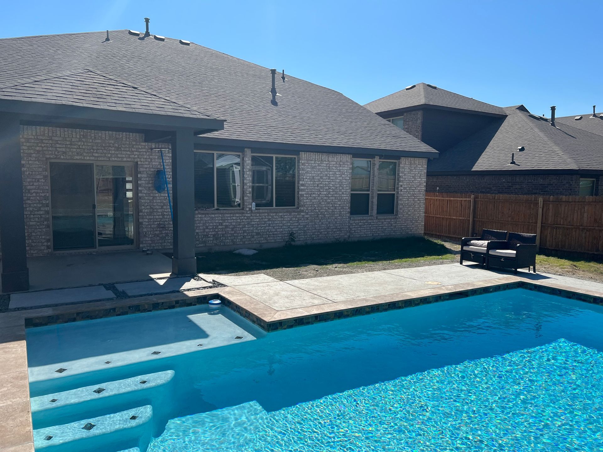 A large swimming pool is in the backyard of a house.