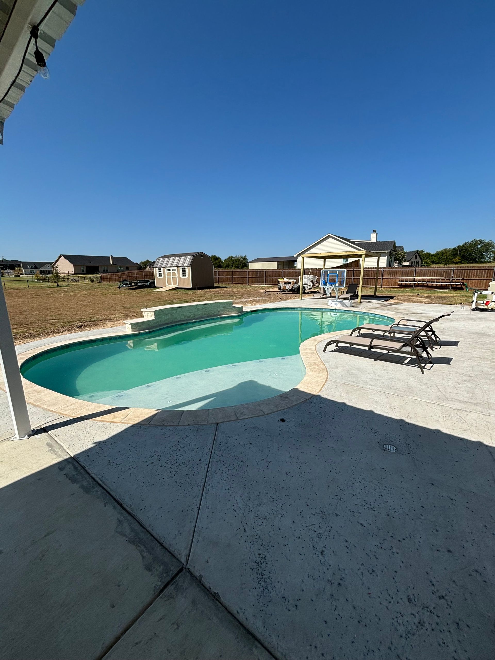 A large swimming pool is surrounded by chairs on a patio