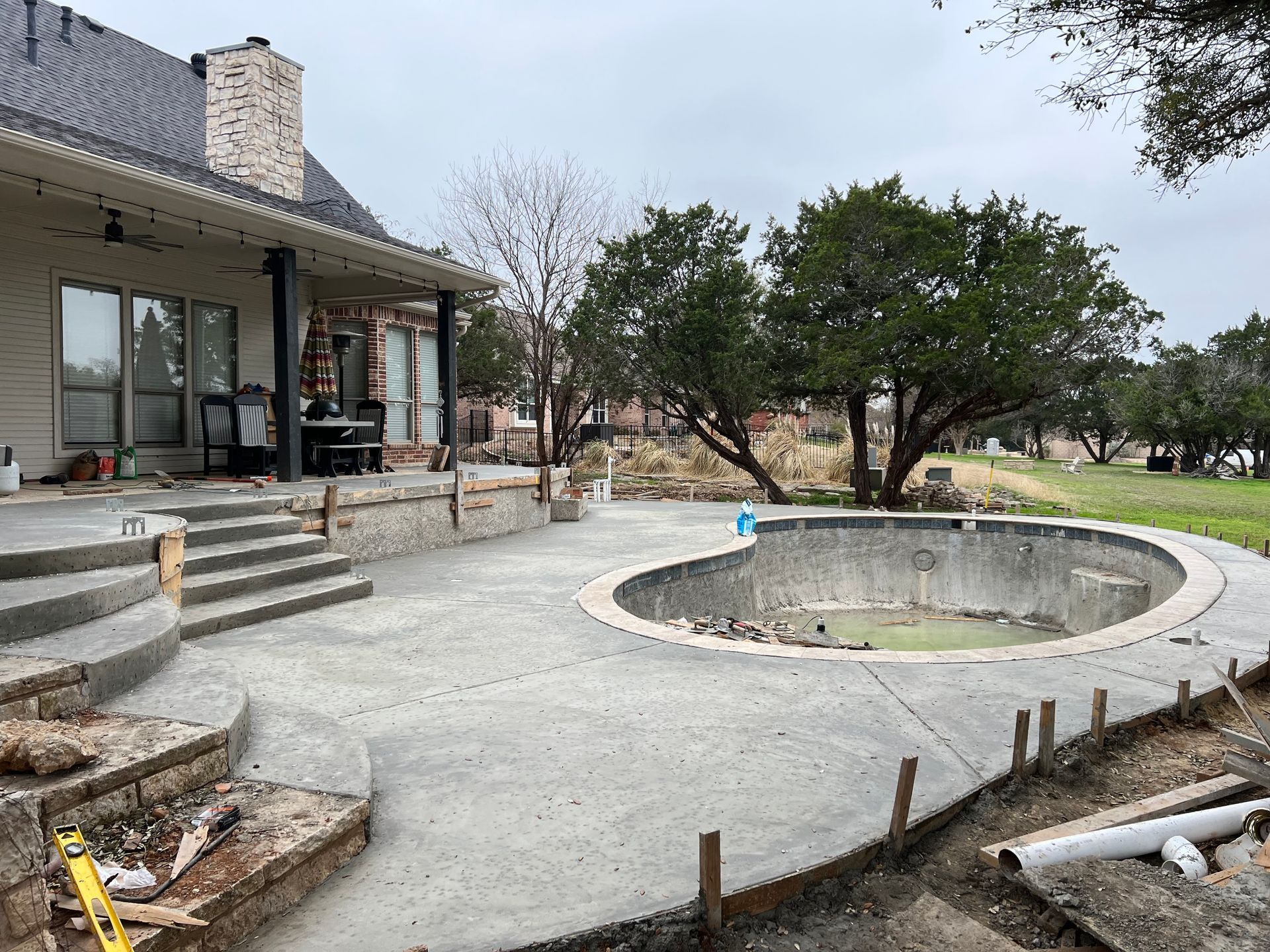A concrete patio with stairs and a pool in the backyard of a house.