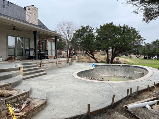 A concrete patio with stairs and a pool in the backyard of a house.