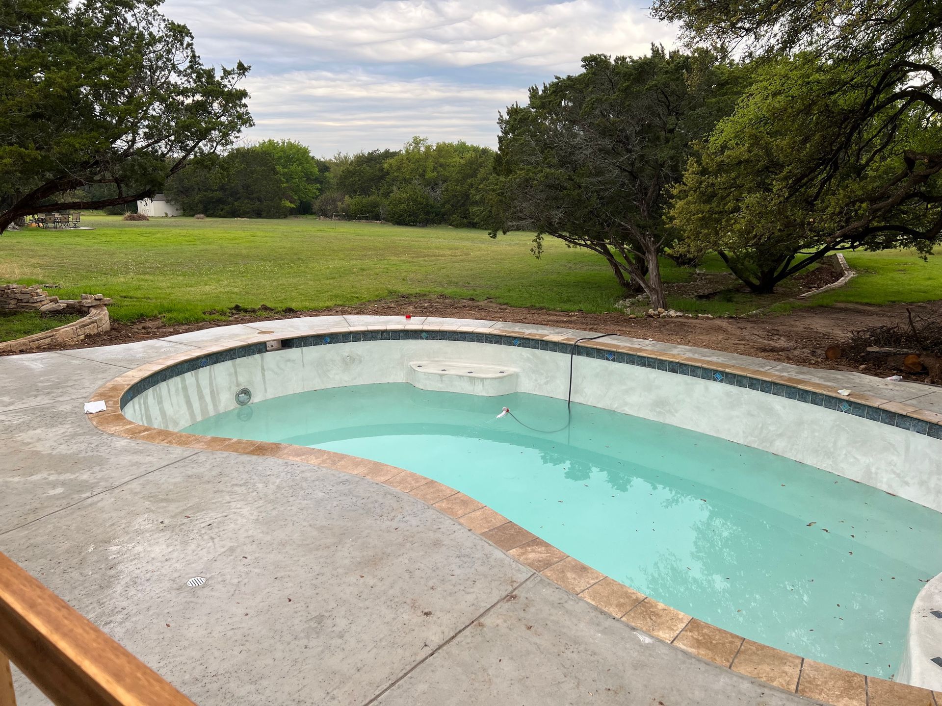 A large swimming pool is surrounded by trees and grass.