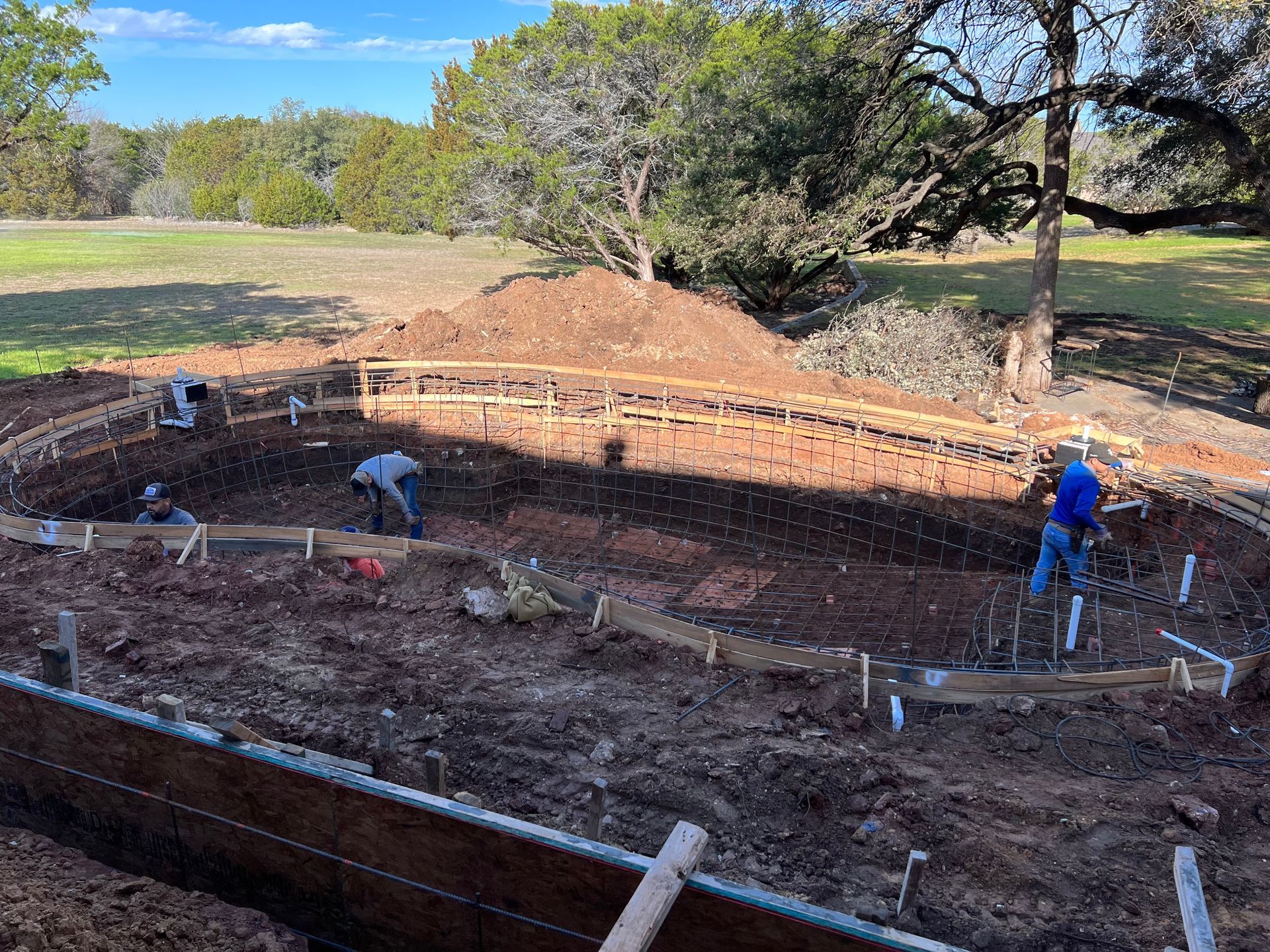 A group of men are working on a swimming pool in the dirt.